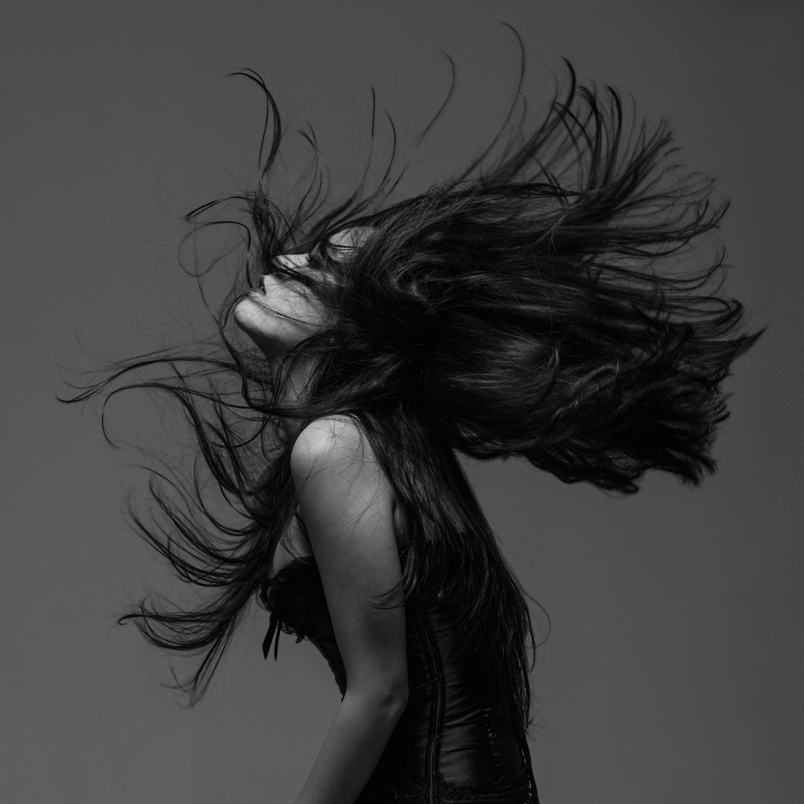 Striking black and white portrait of a woman flipping her hair, captured in a dynamic pose.